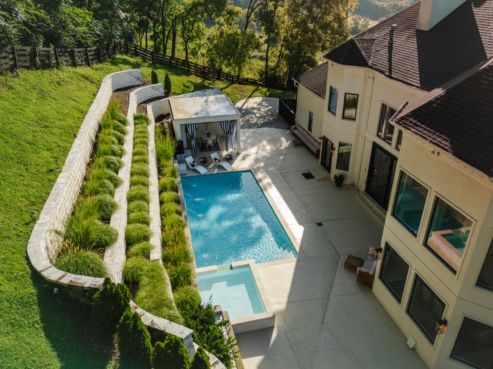 The rear of the estate from the air: the pool, cabana, and terraced grounds below the glass walls.