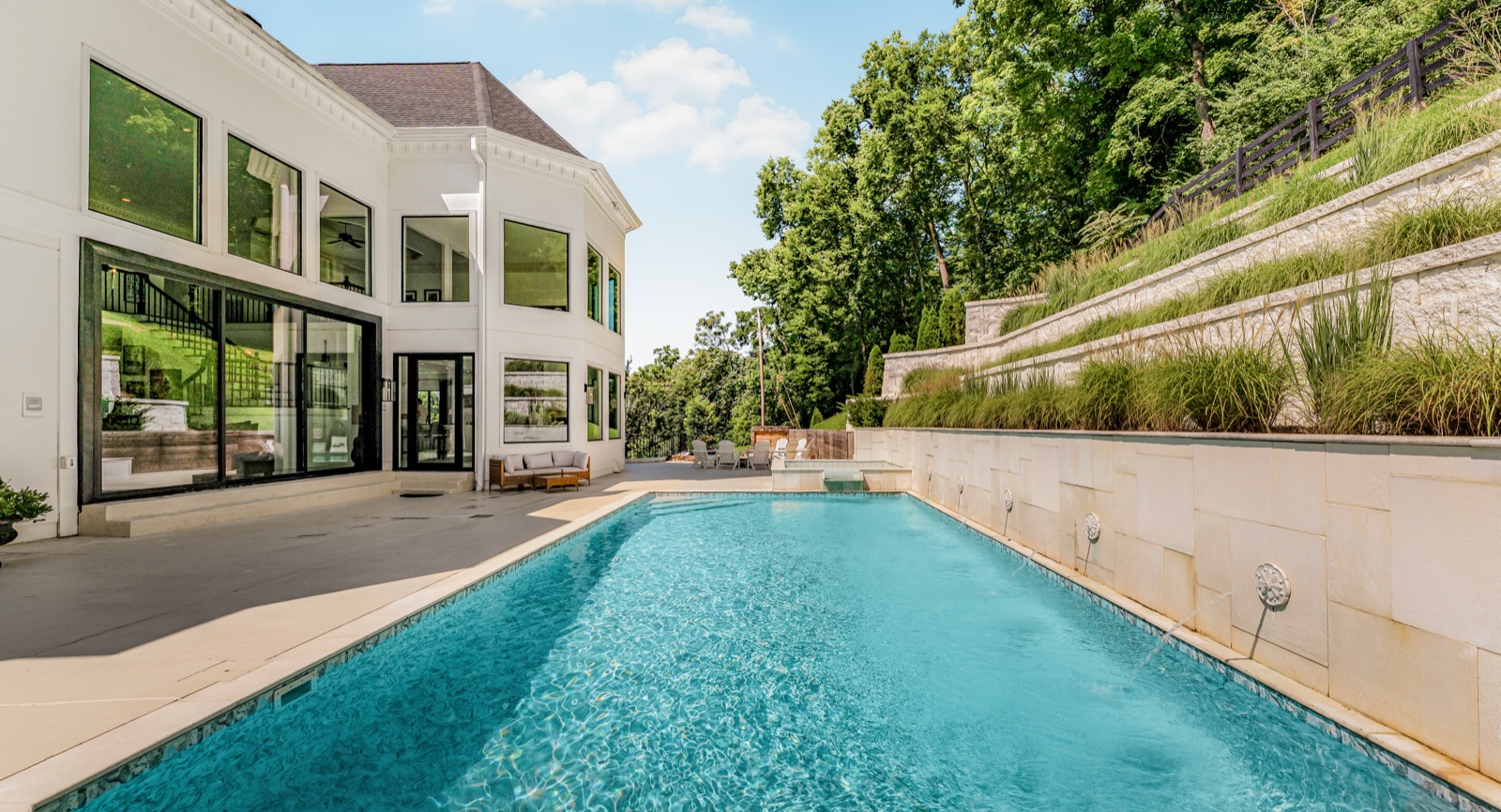 The pool stretched along the rear terrace, the house's glass walls rising at the far end.