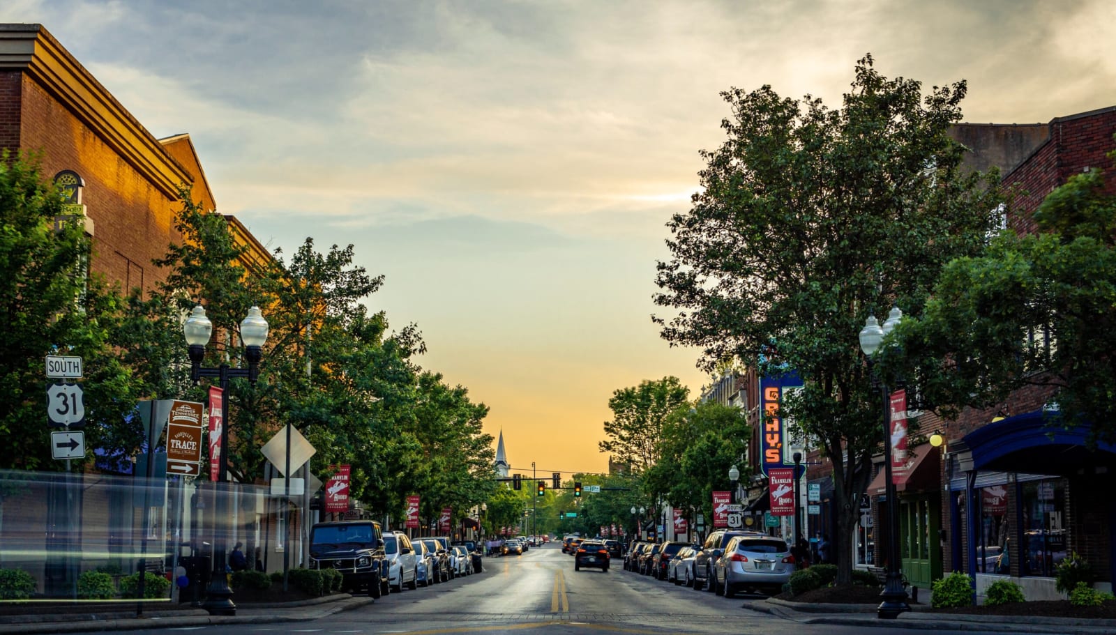 Main Street in downtown Franklin at golden hour: brick storefronts, banners, and the steeple down the block.